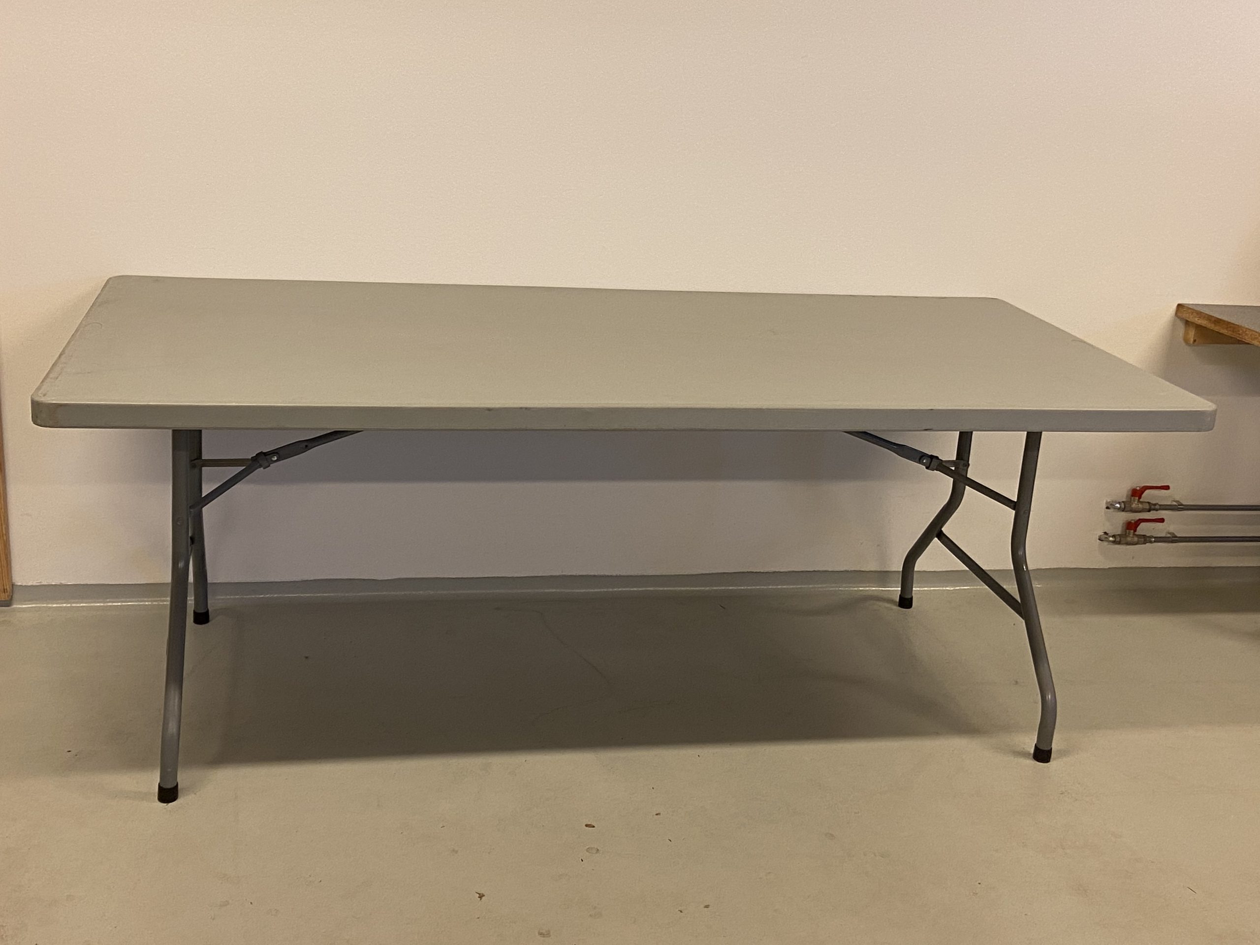 Billedet viser et hvidt plastikbord med stålstel. Det er et 76×180 cm bord
