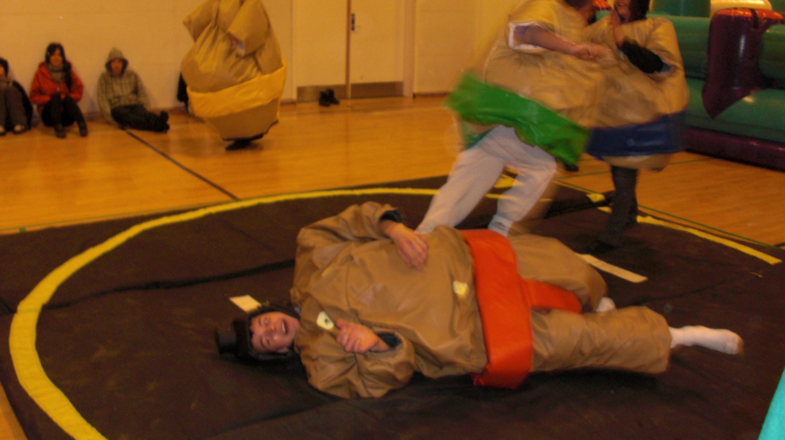 Her ses sumodragter udlejning med to personer der slåsser. De er begge iført en sumodragt og har et hhv. rødt og grønt billede på.